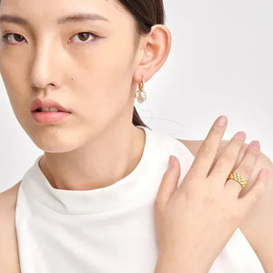 Woman wearing gold-plated hoop earrings and textured gold ring, white sleeveless top