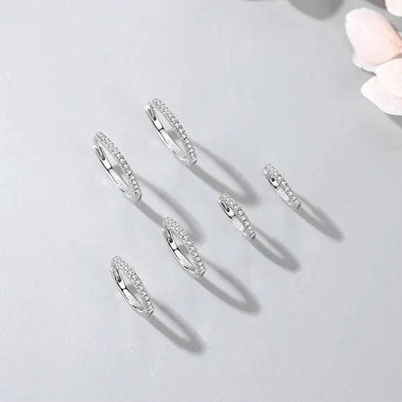 Set of silver hoop earrings on a light gray background with a soft pink flower.