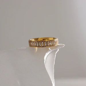 18K gold-plated ring with baguette-cut clear stones on a white textured surface