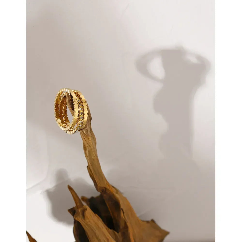 Gold-plated textured ring displayed on driftwood with artistic shadow on white background