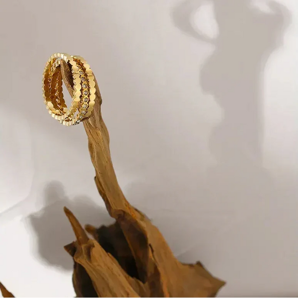 Gold-plated textured ring displayed on driftwood with artistic shadow on white background