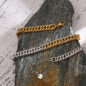Three chain bracelets in gold, silver, and bronze on a textured stone surface.
