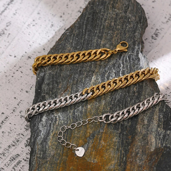 Three chain bracelets in gold, silver, and bronze on a textured stone surface.