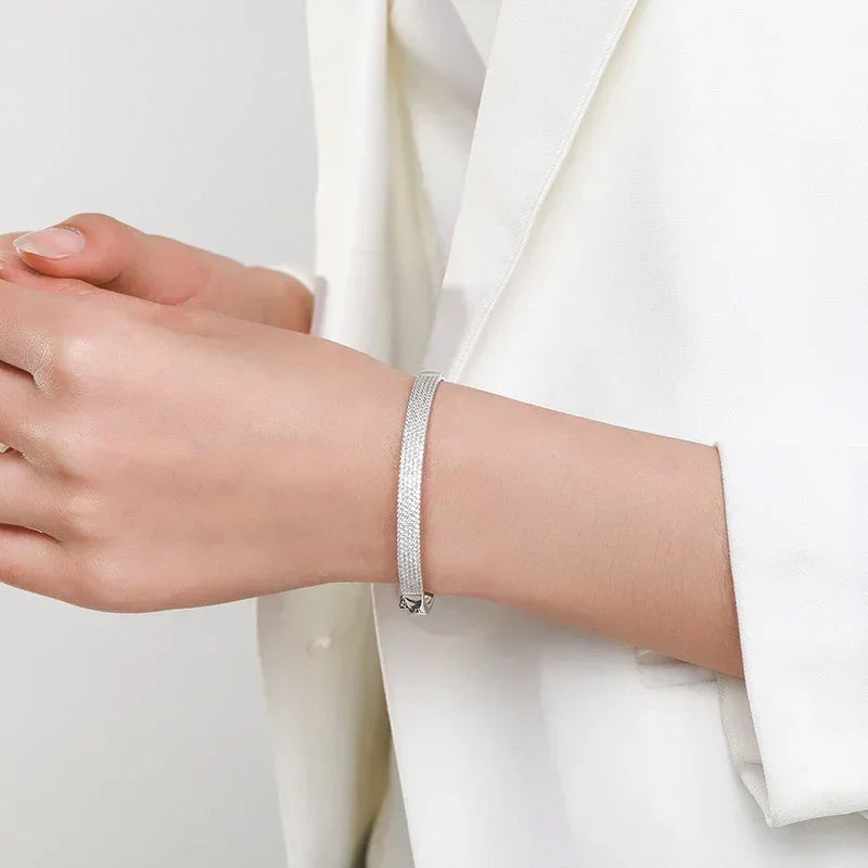 Elegant woman wearing minimalist 925 silver bracelet with fine texture, white blazer background.