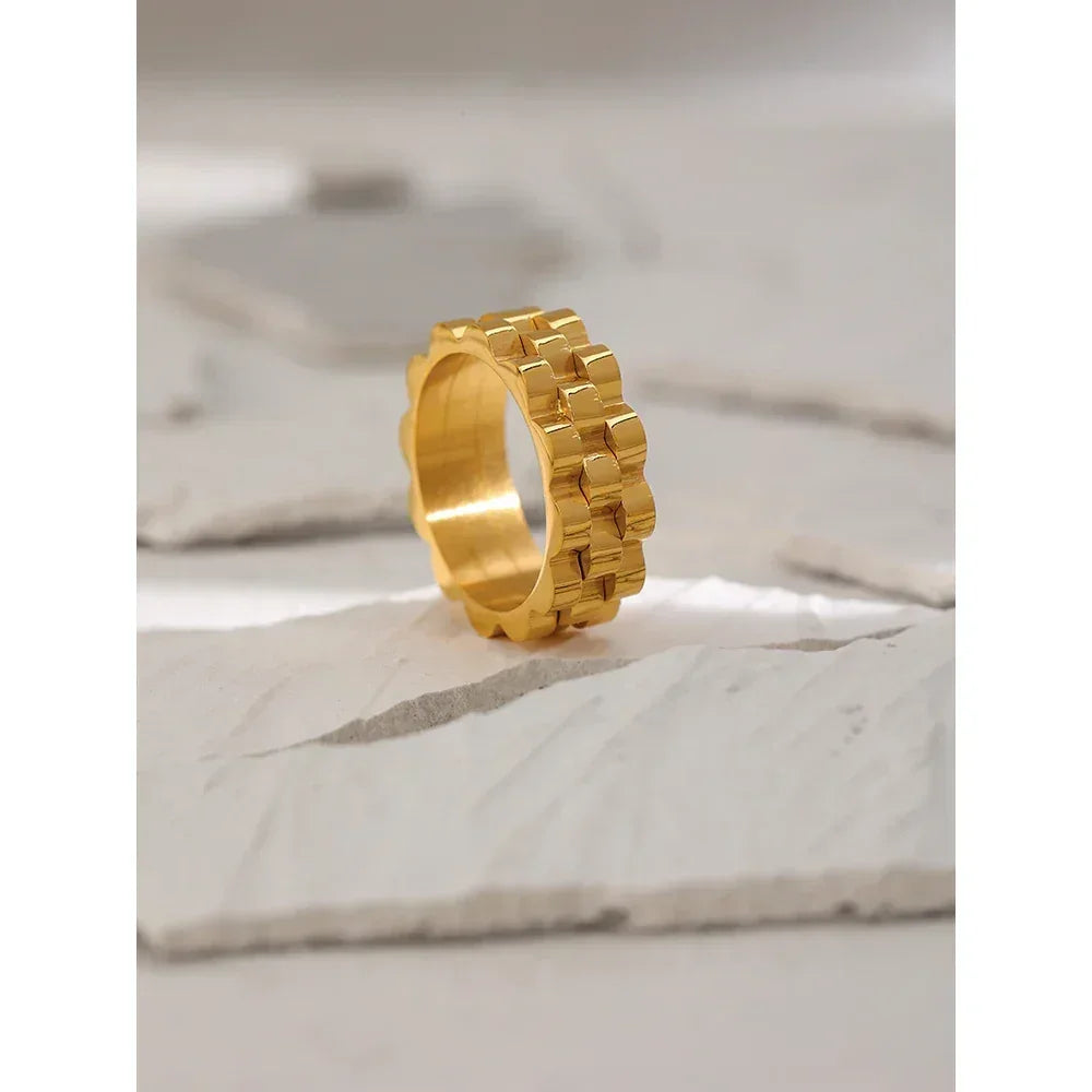 Chunky 18K gold-plated ring with geometric link design on a textured stone background