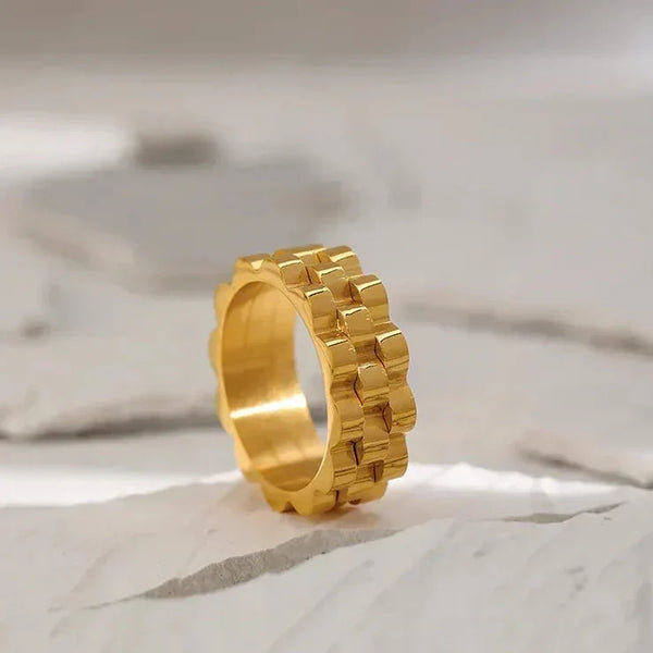 Chunky 18K gold-plated ring with geometric link design on a textured stone background