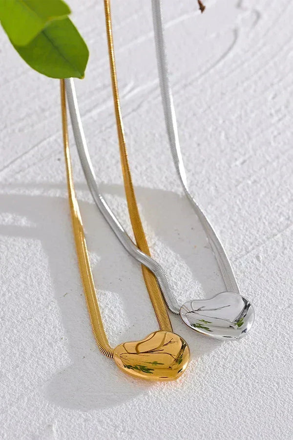 Gold and silver necklaces on a textured white surface with a green leaf.
