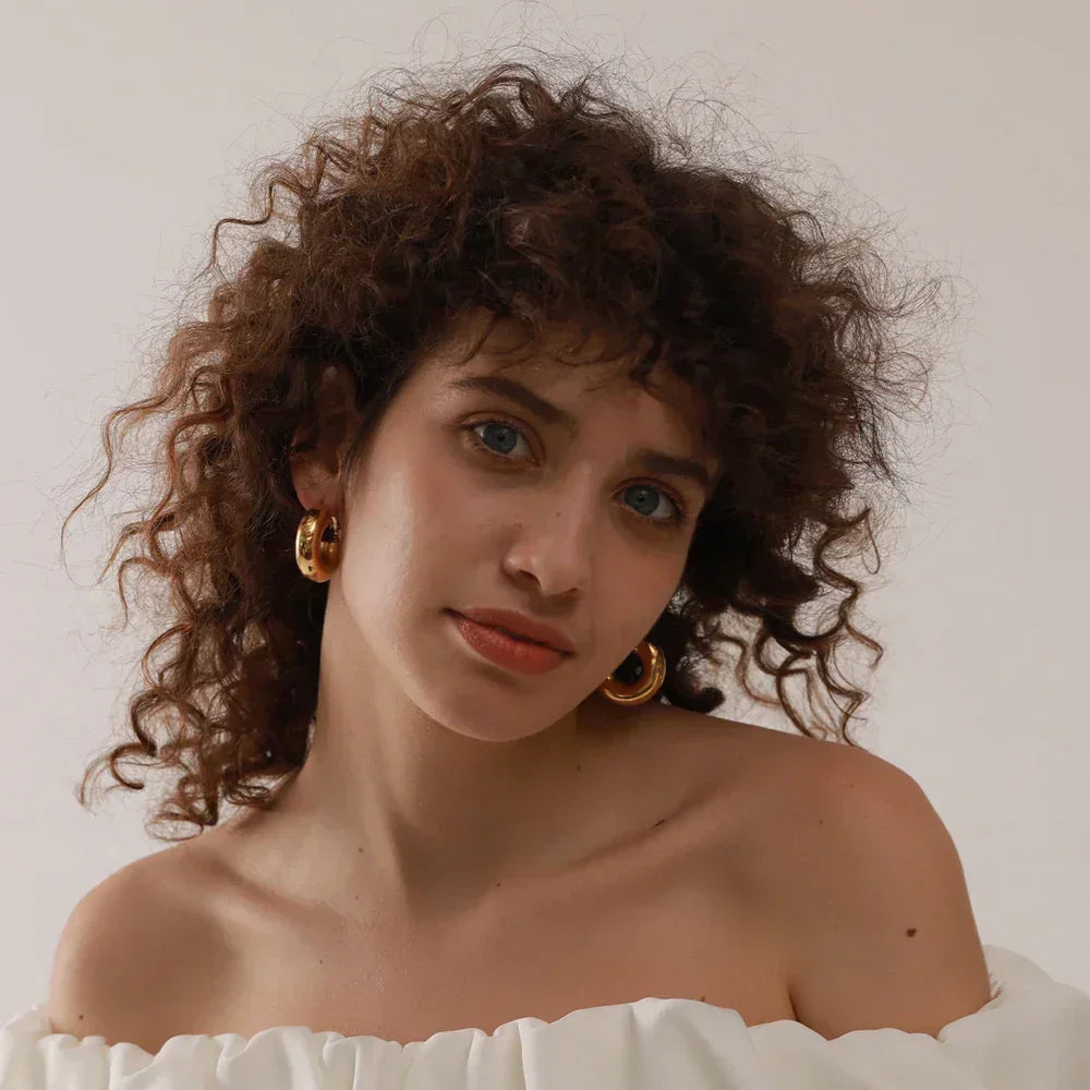 Woman with curly hair wearing chunky gold hoop earrings and an off-shoulder white top