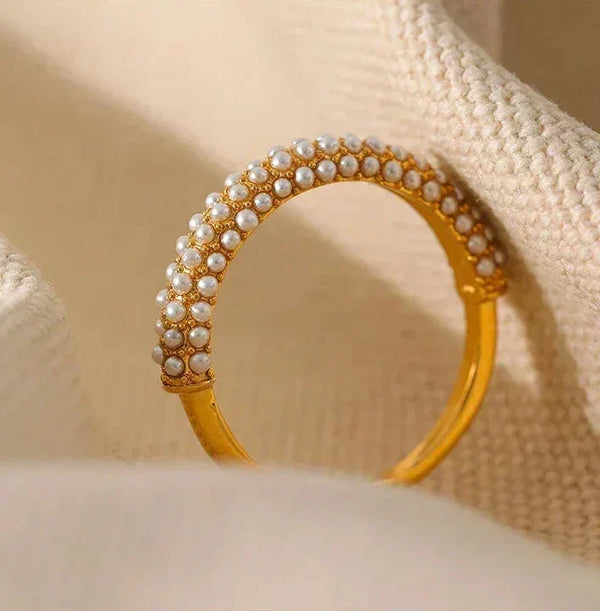 Gold-plated ring with rows of small pearls on textured beige fabric background