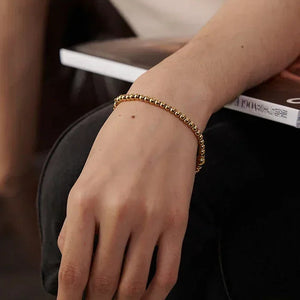 Woman wearing elegant 18K gold-plated beaded bracelet, holding a magazine