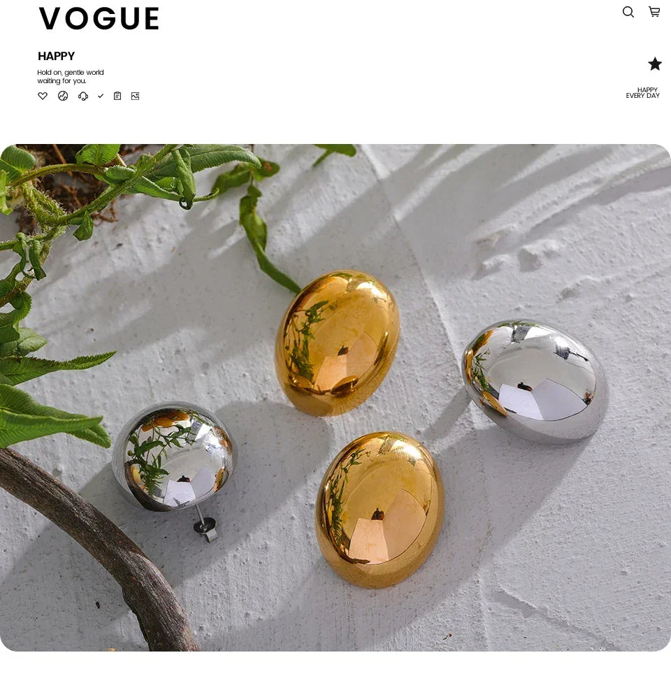 Gold and silver oval jewelry pieces on textured white surface with green leaves