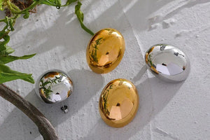 Gold and silver oval jewelry pieces on textured white surface with green leaves