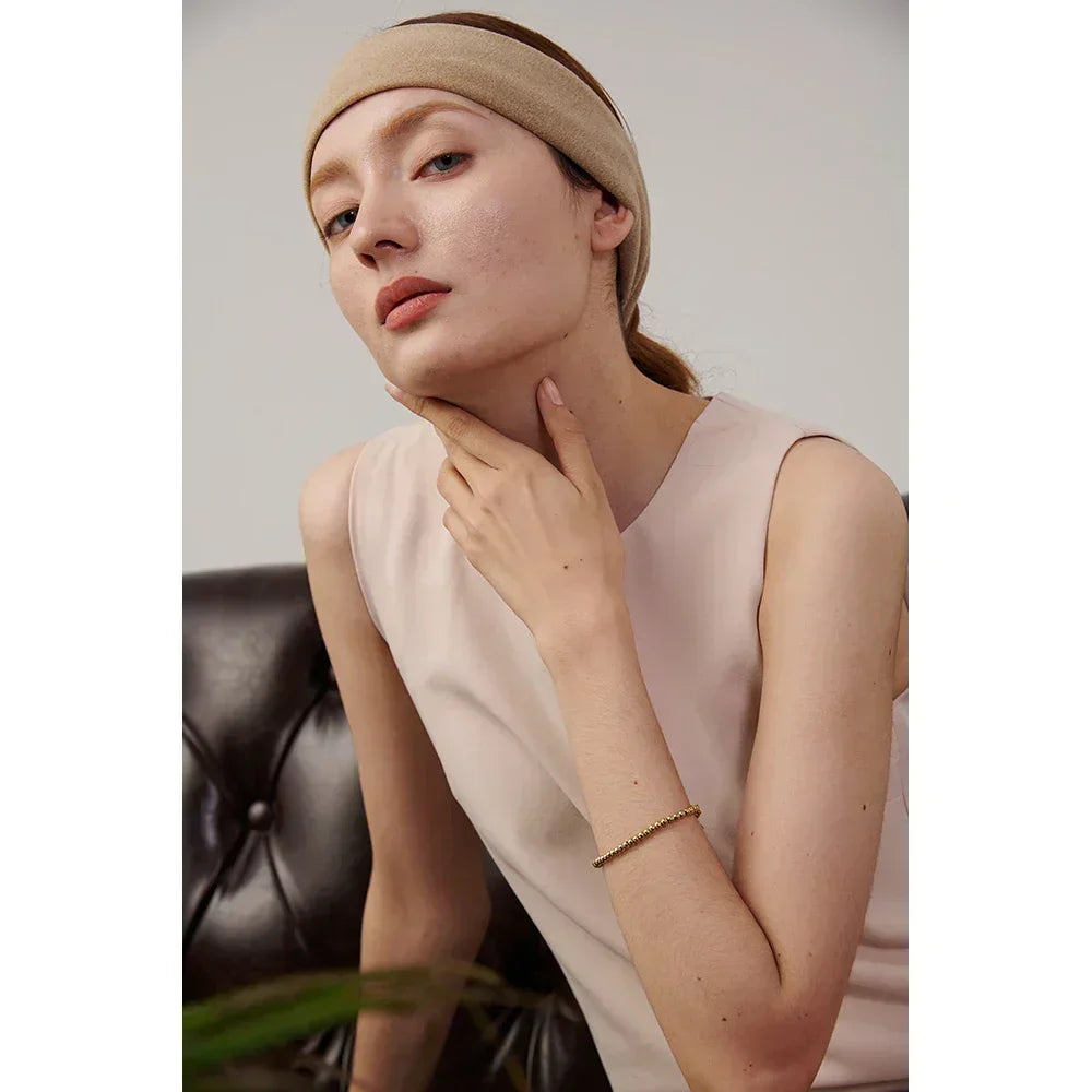 Woman in beige headband and sleeveless top wearing delicate gold-plated bracelet