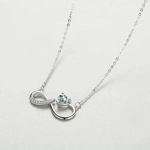 Silver necklace with a heart and infinity symbol pendant on a light gray background