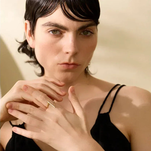 Woman in black dress wearing gold-plated zigzag ring on hand, elegant jewelry close-up