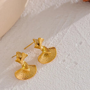 Gold earrings on a textured white surface with 'Vogue' branding.