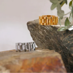 Silver and gold chunky chain rings on textured fabric with natural stone background
