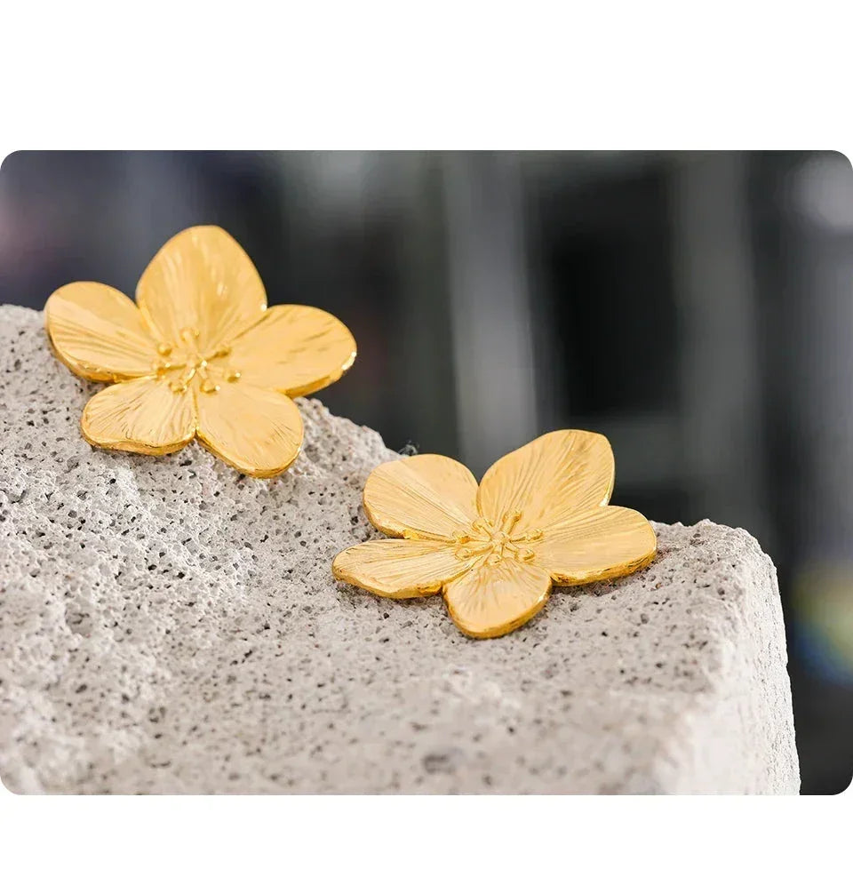 Gold-plated flower stud earrings displayed on a textured stone surface