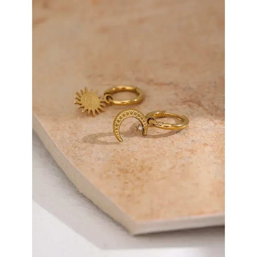 Gold-plated hoop earrings with sun and crescent moon charms on a stone surface