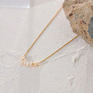 Gold-plated necklace with seven freshwater pearls on sandy textured background