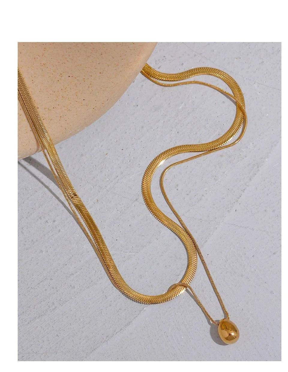 18K gold-plated herringbone chain necklace with teardrop pendant on light surface