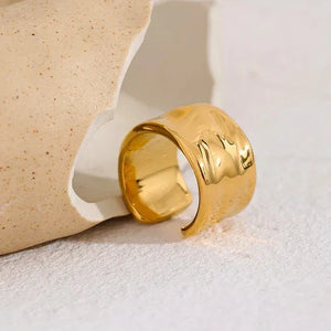 Wide gold-plated adjustable ring with hammered texture on neutral stone background