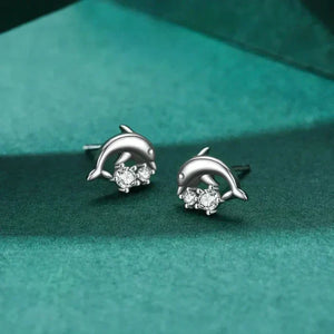 Silver dolphin earrings with embedded stones on a teal fabric background