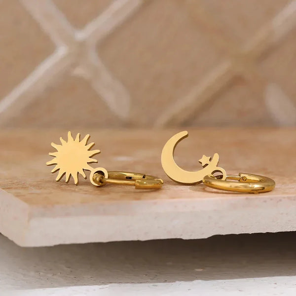 Gold sun and moon earrings on a marble surface with a neutral background