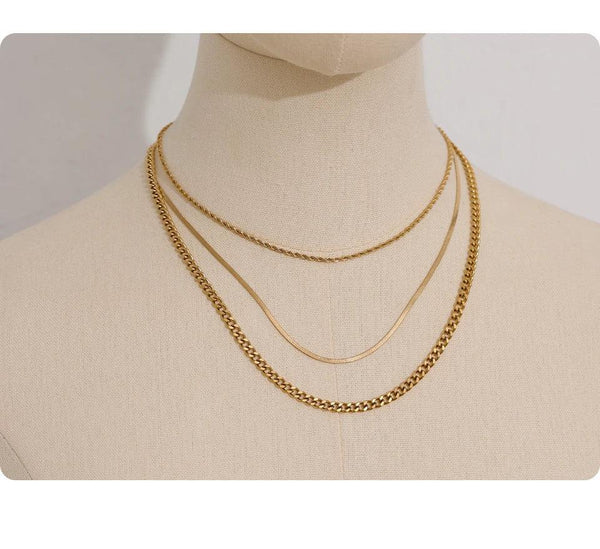 Layered gold-plated chain necklaces displayed on a beige mannequin bust