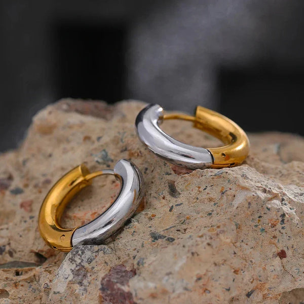 Two gold and silver hoop earrings on a textured stone surface with a blurred background.