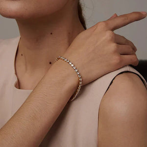Woman wearing a beige headband and bracelet, pointing to her wrist.