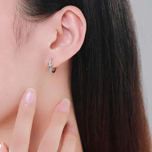 Close-up of an ear wearing a silver earring with a hand adjusting it against a neutral background