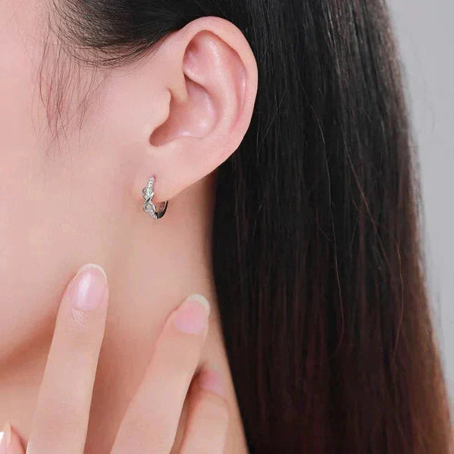 Close-up of an ear wearing a silver earring with a hand adjusting it against a neutral background