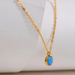 Gold necklace with a blue pendant on a white background, featuring the Vogue logo.