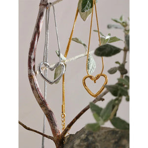 Silver and gold heart pendant necklaces displayed on a natural tree branch.