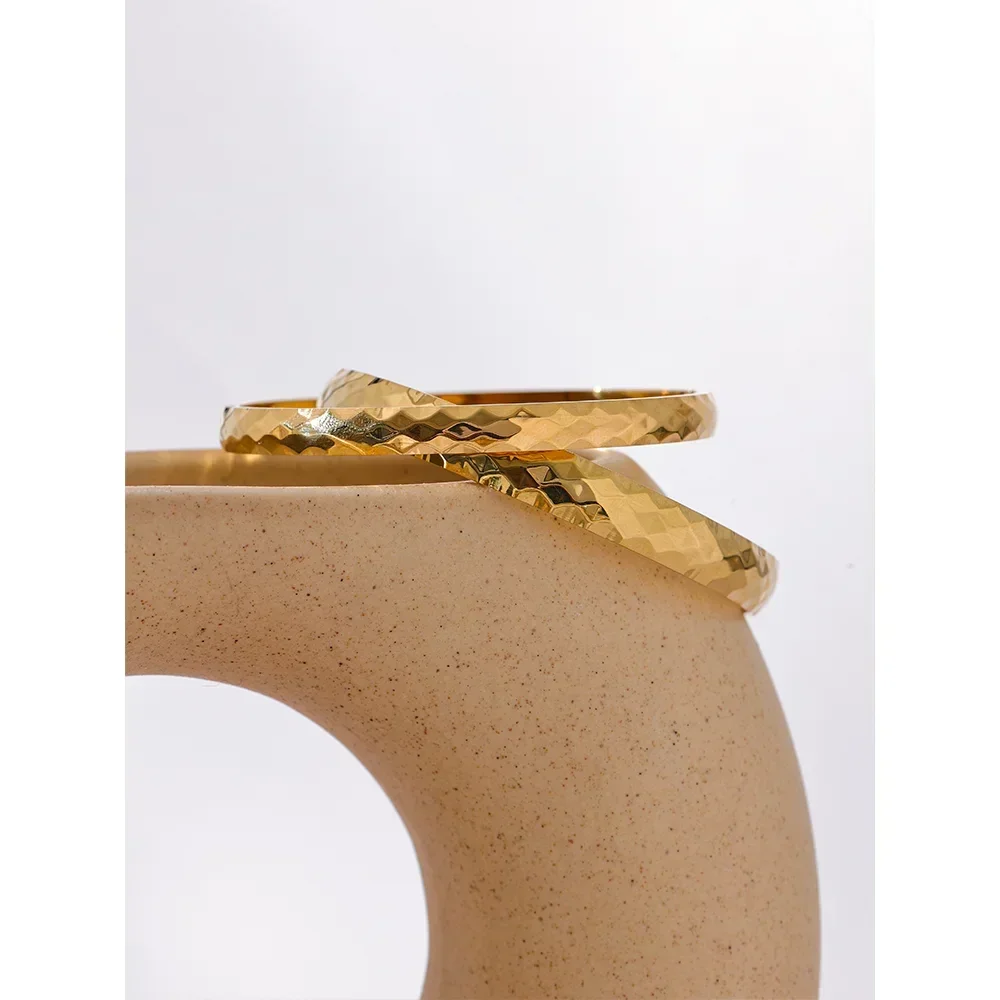 Pair of hammered 18K gold-plated bangles displayed on a curved ceramic stand
