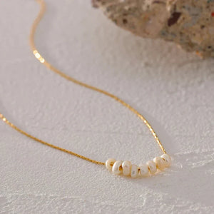 Gold necklace with pearls on a textured surface, branded 'Vogue'.