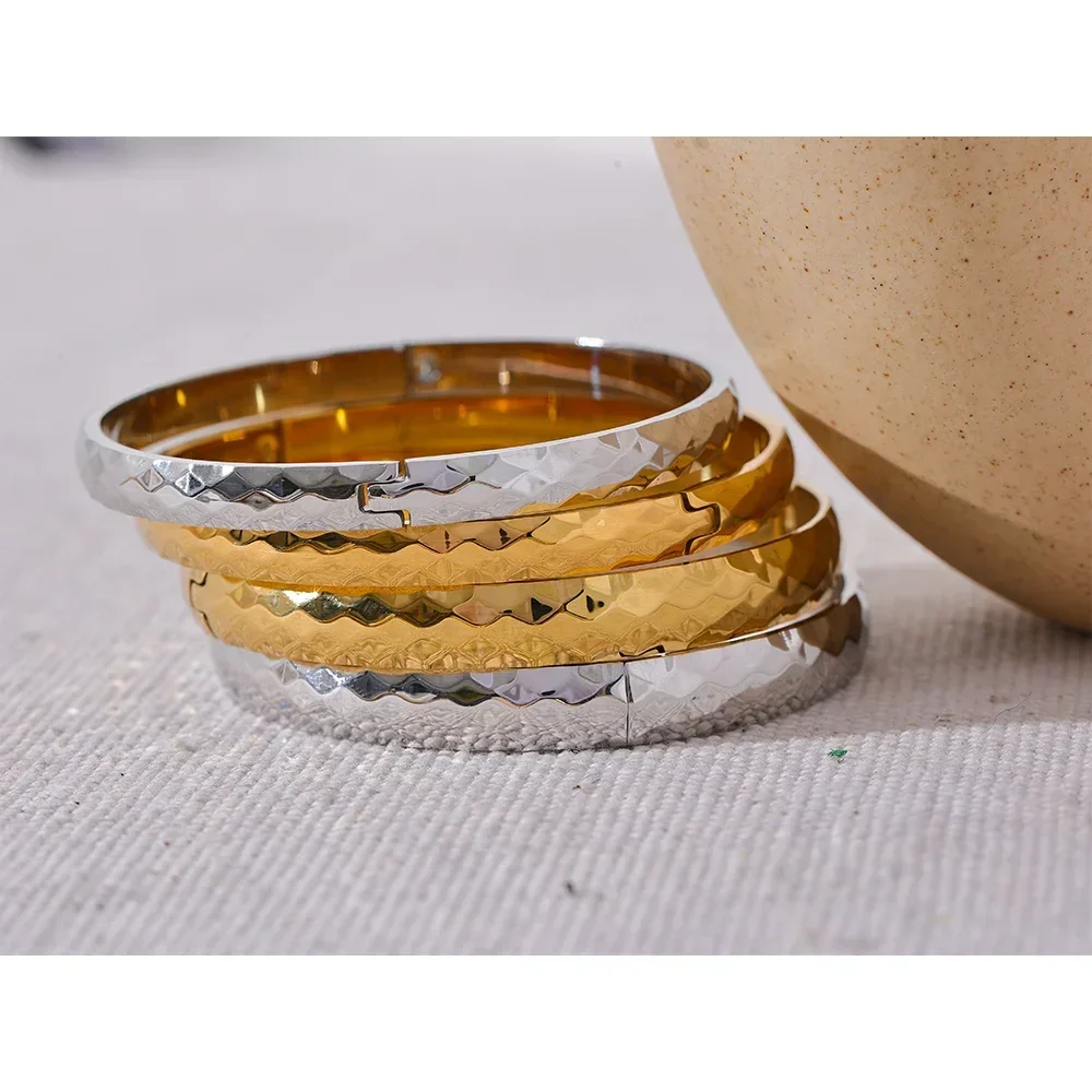 Stack of hammered 925 silver and gold-plated bangles on a textured white surface