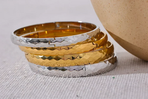 Stack of hammered steel and gold-plated bangles on a textured white surface
