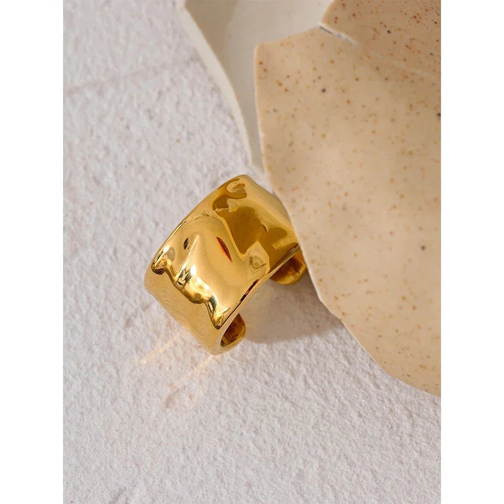 Wide gold-plated ring with hammered texture on a light textured background