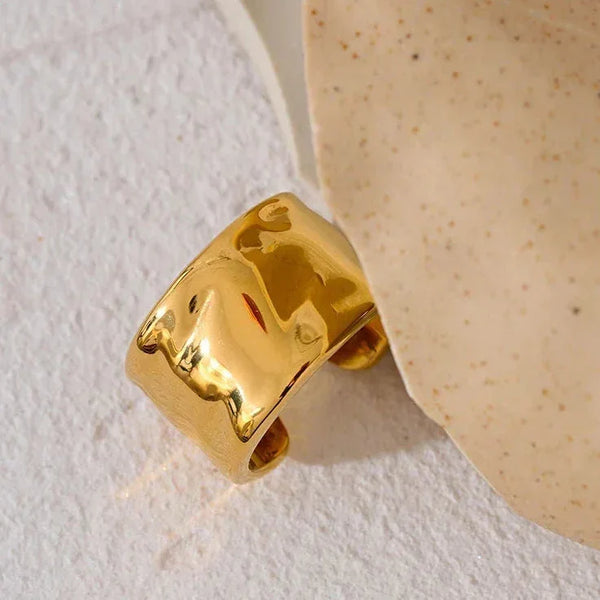 Wide gold-plated ring with hammered texture on a light textured background