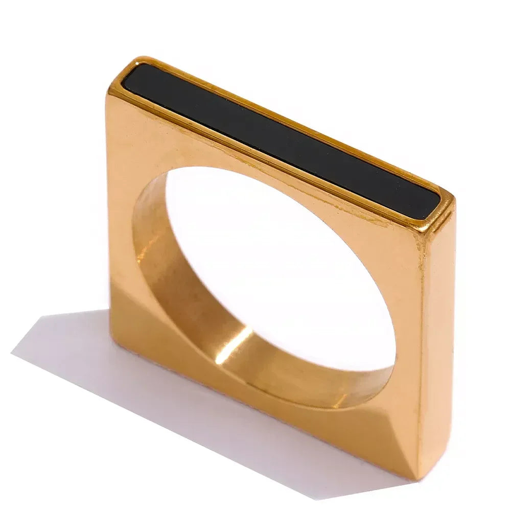 Square gold-plated ring with black enamel accent, modern geometric jewelry design on white background.