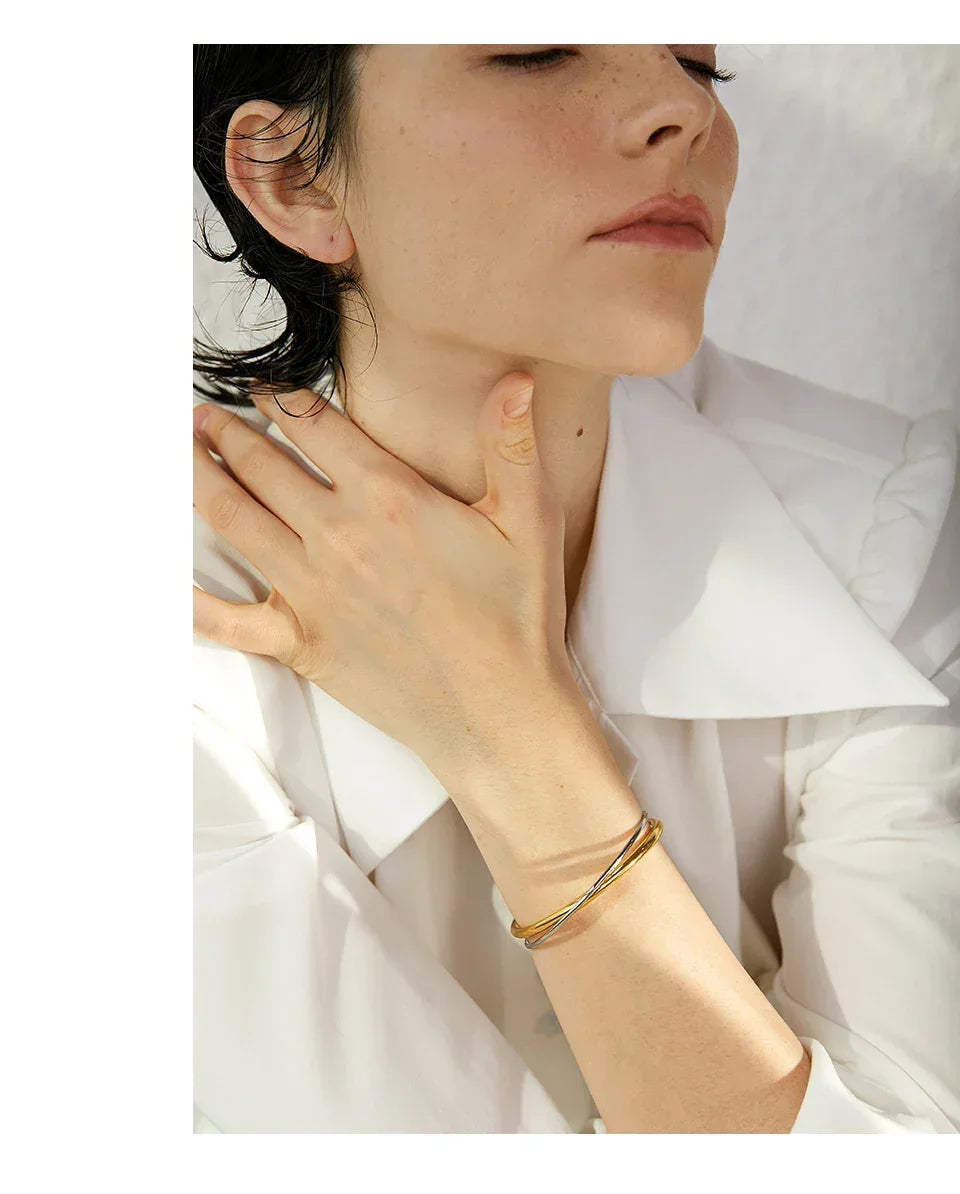 Woman wearing minimalist 18K gold-plated and silver bangle bracelet, white blouse