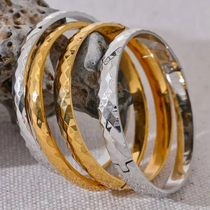 Stacked hammered steel and gold-plated bangles on textured stone, elegant jewelry