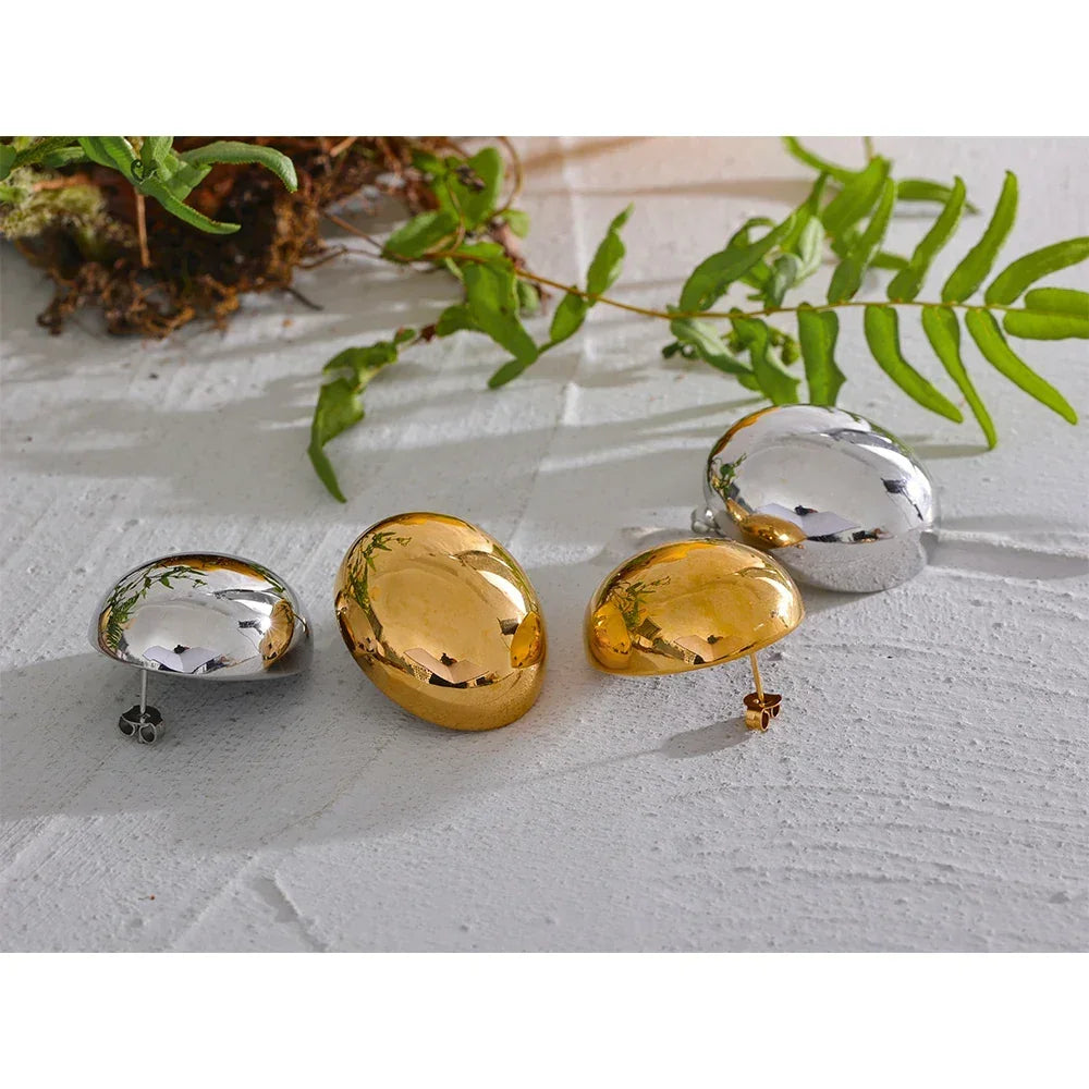 Set of polished 925 silver and 18K gold-plated oval stud earrings on white surface with green leaves