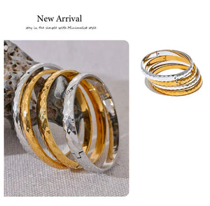Stacked hammered steel and gold-plated bangles on textured stone, elegant jewelry