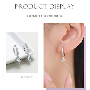 Sparkling Hoop Earrings - TM & CO. JEWELS - Silver hoop earrings with heart-shaped gemstones displayed on a white surface and worn by a person.