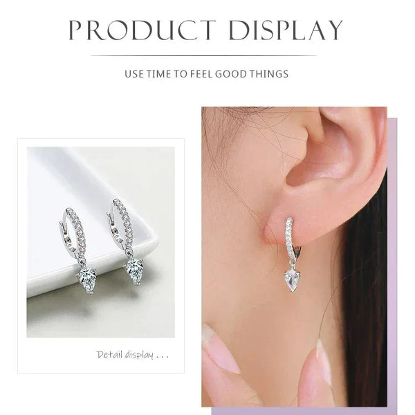 Sparkling Hoop Earrings - TM & CO. JEWELS - Silver hoop earrings with heart-shaped gemstones displayed on a white surface and worn by a person.