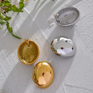 Gold and silver oval locket pendants with textured and polished finishes on a white surface