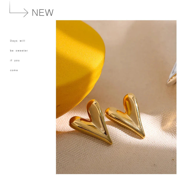 Gold heart-shaped earrings on a beige surface with a yellow object in the background.